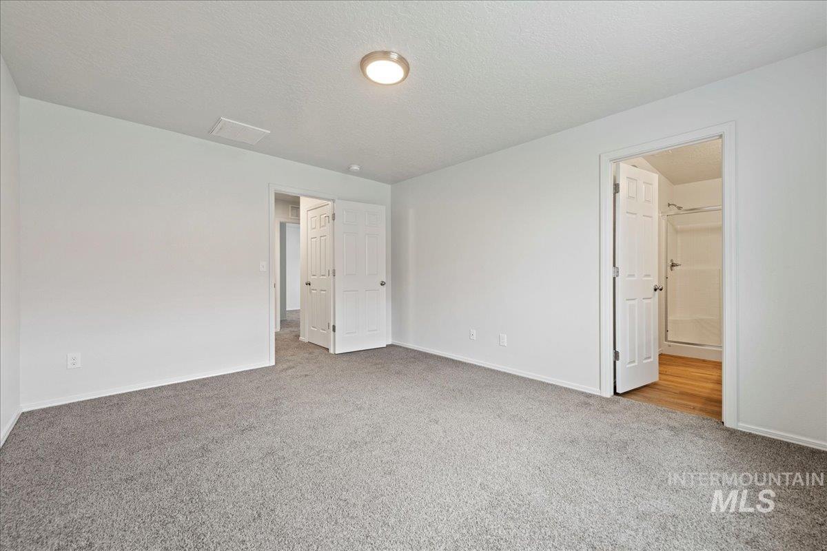 Unfurnished bedroom with light carpet, a textured ceiling, and connected bathroom