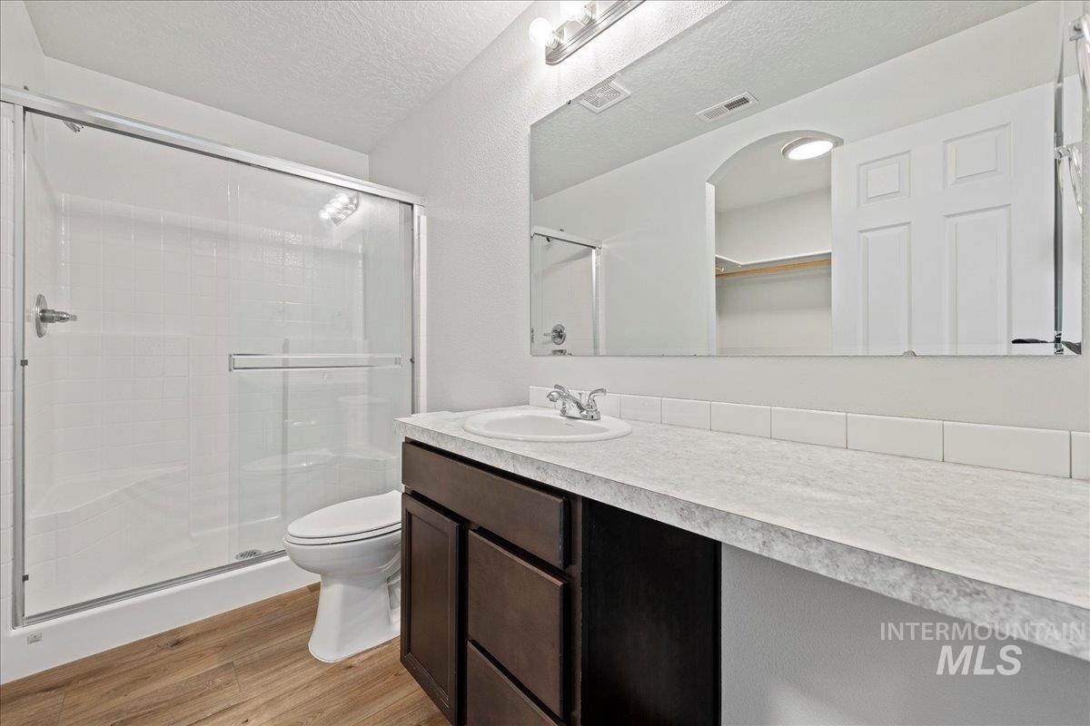 Bathroom featuring light wood-style flooring, vanity, a shower stall, a textured ceiling, and a walk in closet