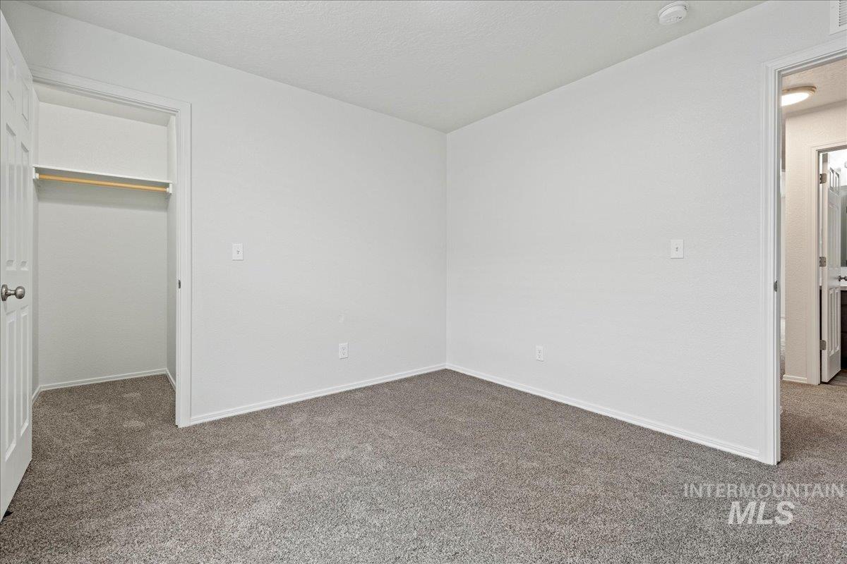 Unfurnished bedroom featuring carpet flooring, a walk in closet, and a textured ceiling
