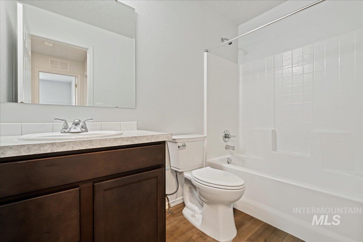Full bath featuring vanity, shower / tub combination, wood finished floors, and a textured wall