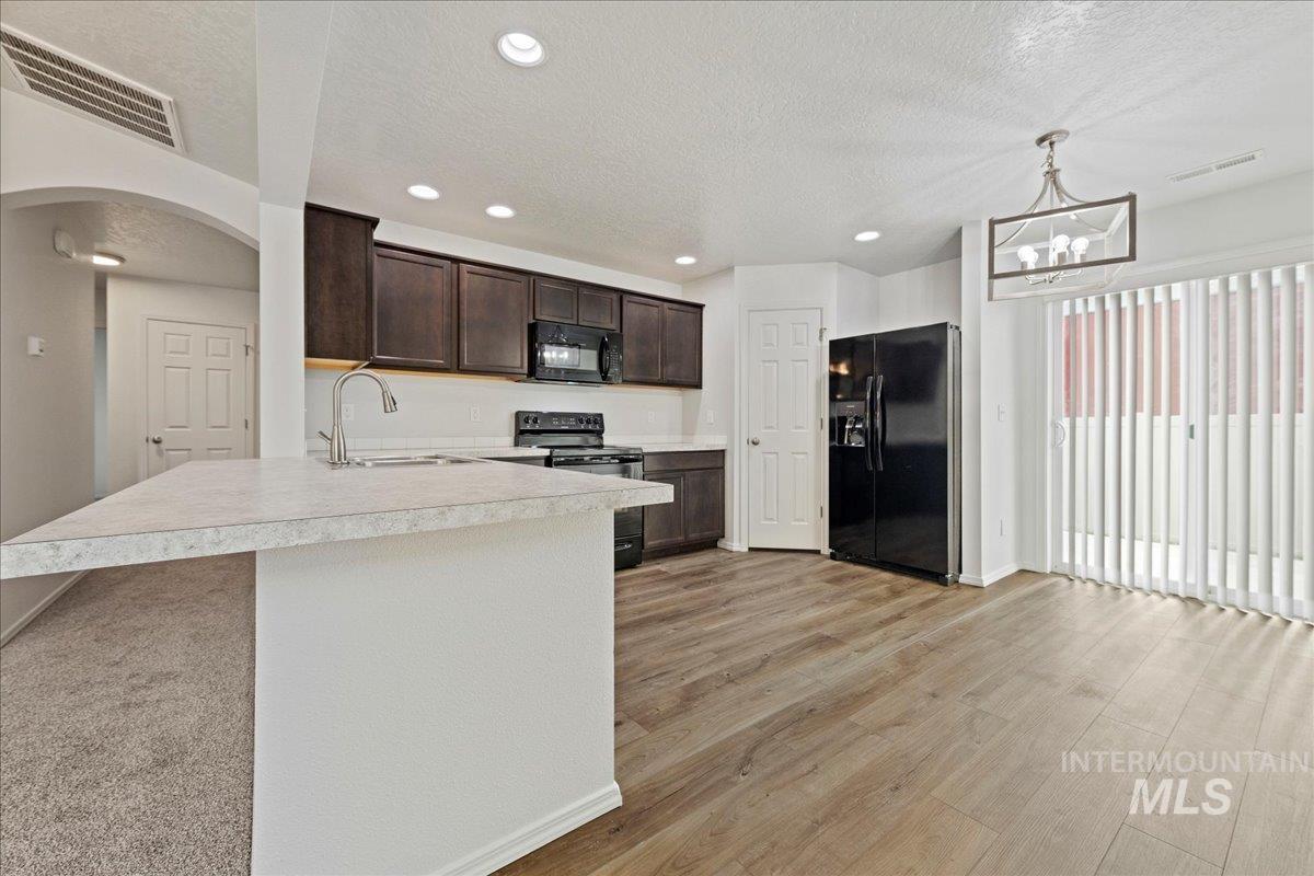 Kitchen with dark brown cabinets, light countertops, black appliances, a textured ceiling, and arched walkways