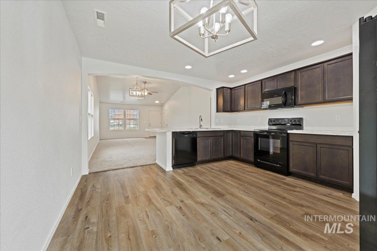 Kitchen featuring a chandelier, light countertops, dark brown cabinets, black appliances, and open floor plan