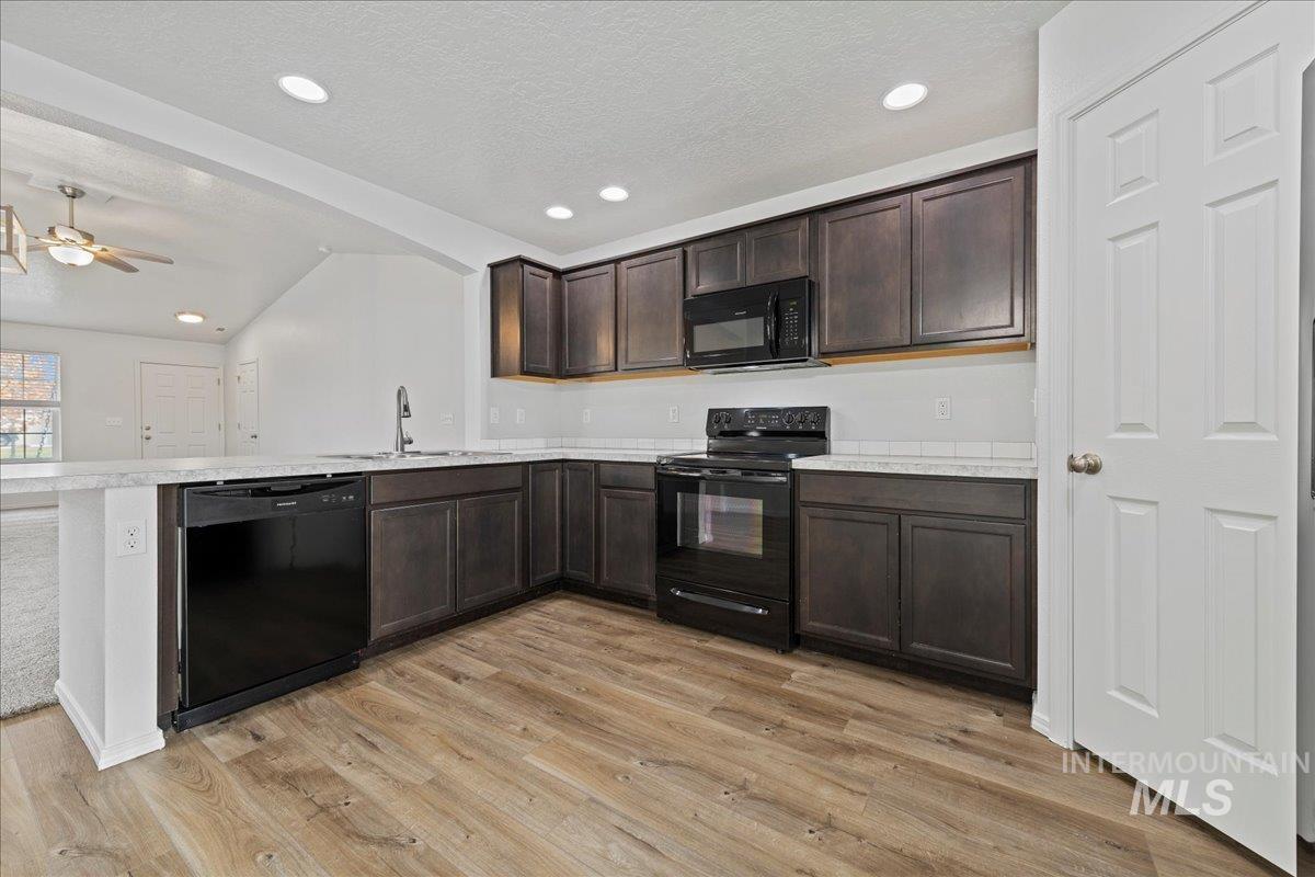 Kitchen featuring dark brown cabinets, light countertops, black appliances, recessed lighting, and light wood-style flooring