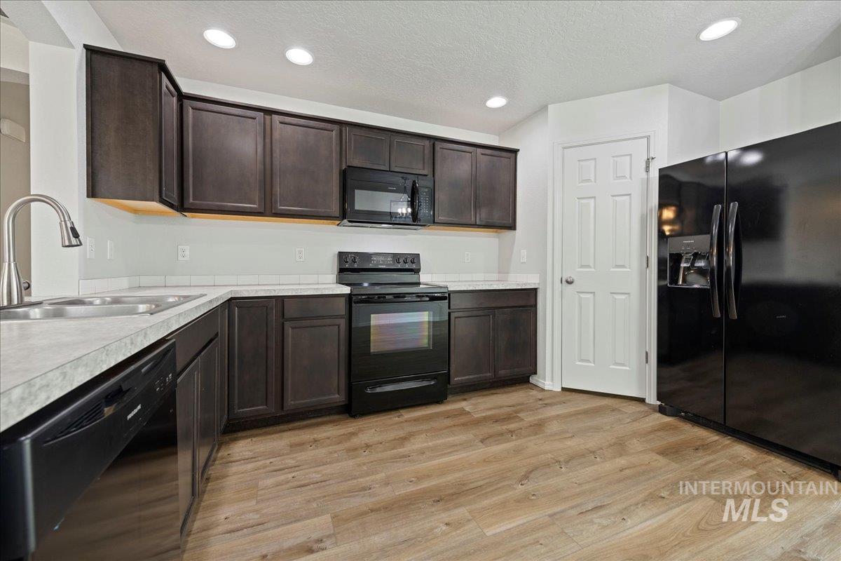 Kitchen featuring black appliances, dark brown cabinetry, recessed lighting, light countertops, and light wood finished floors