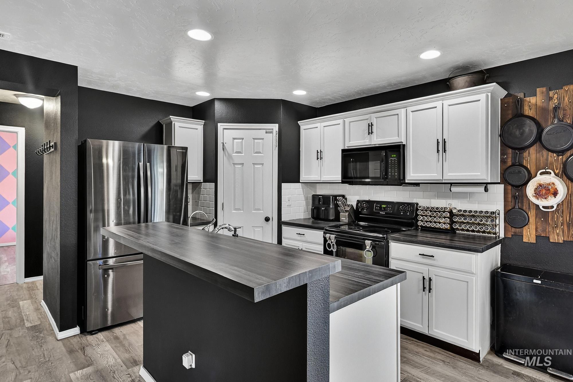 Kitchen featuring black appliances, a center island, white cabinetry, a textured ceiling, and laminate wood-type flooring