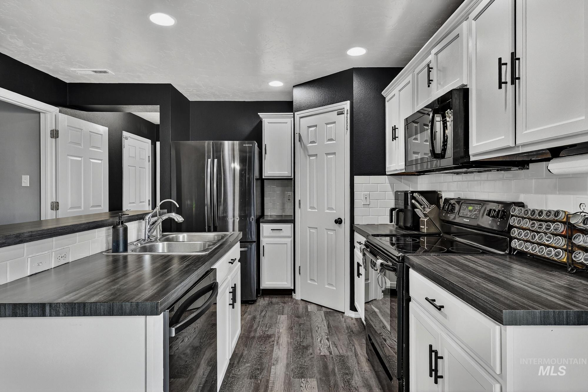 Kitchen featuring black appliances, backsplash, white cabinets, laminate wood-type flooring, and recessed lighting