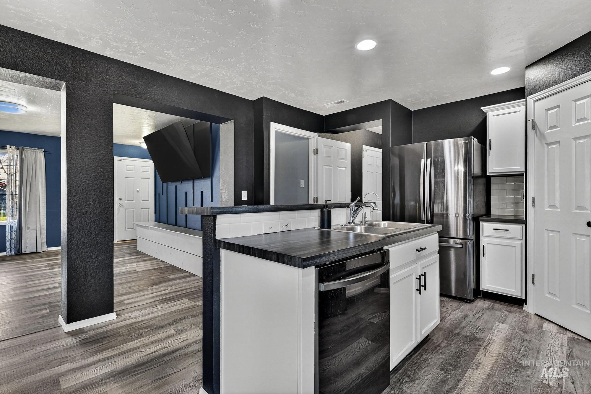 Kitchen with dark countertops, white cabinetry, an island with sink, freestanding refrigerator, and a textured ceiling