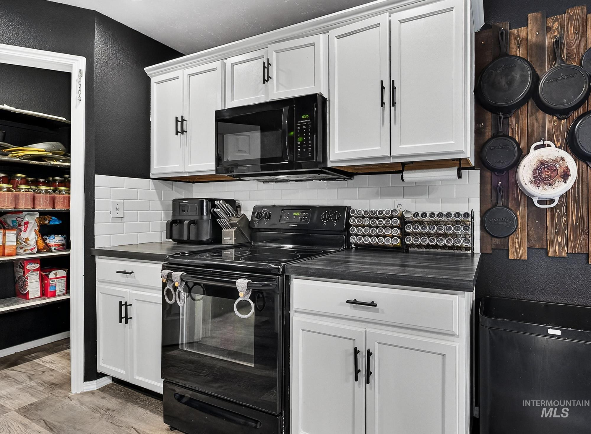 Kitchen with black appliances, dark countertops, white cabinets, a textured wall, and backsplash