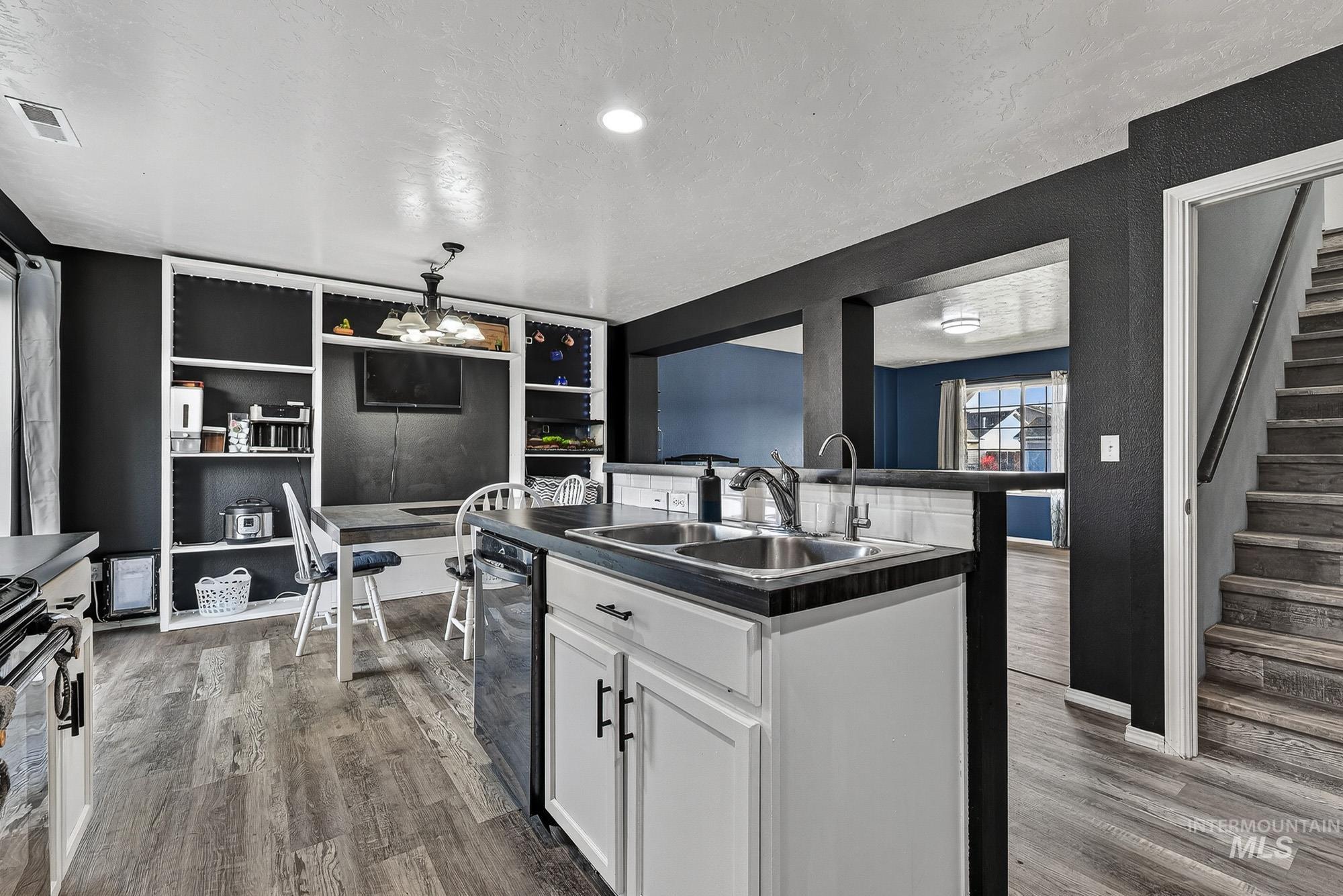 Kitchen with white cabinetry, a textured ceiling, an island with sink, dark countertops, and laminate wood-type flooring