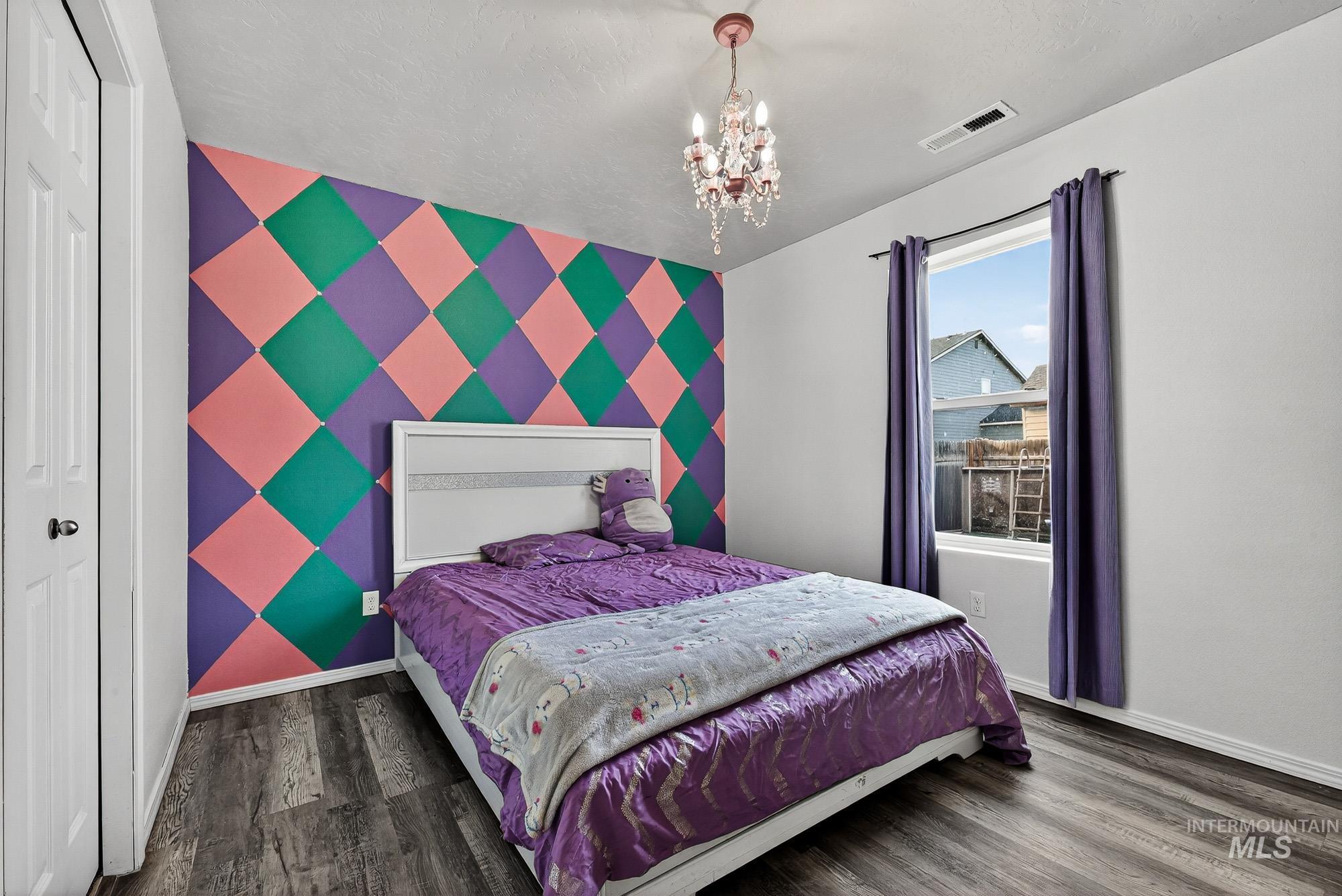 Bedroom with an accent wall, a chandelier, laminate wood-style floors, a closet, and wallpapered walls