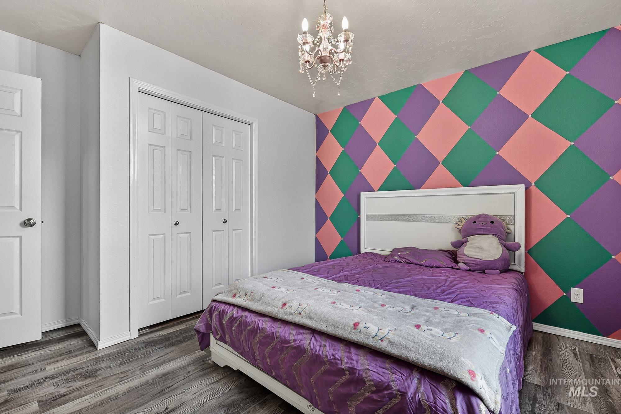 Bedroom featuring an accent wall, a chandelier, laminate wood -like finished floors, and a closet