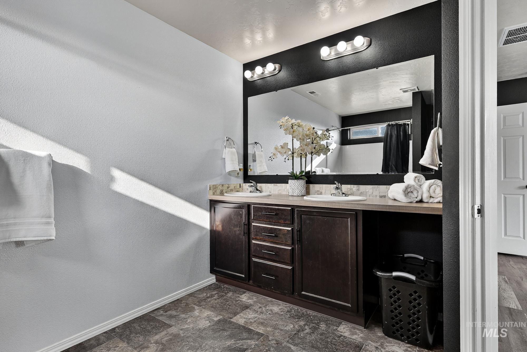 Primary Full bath featuring double vanity, a textured wall, and woodlike laminate finished flooring