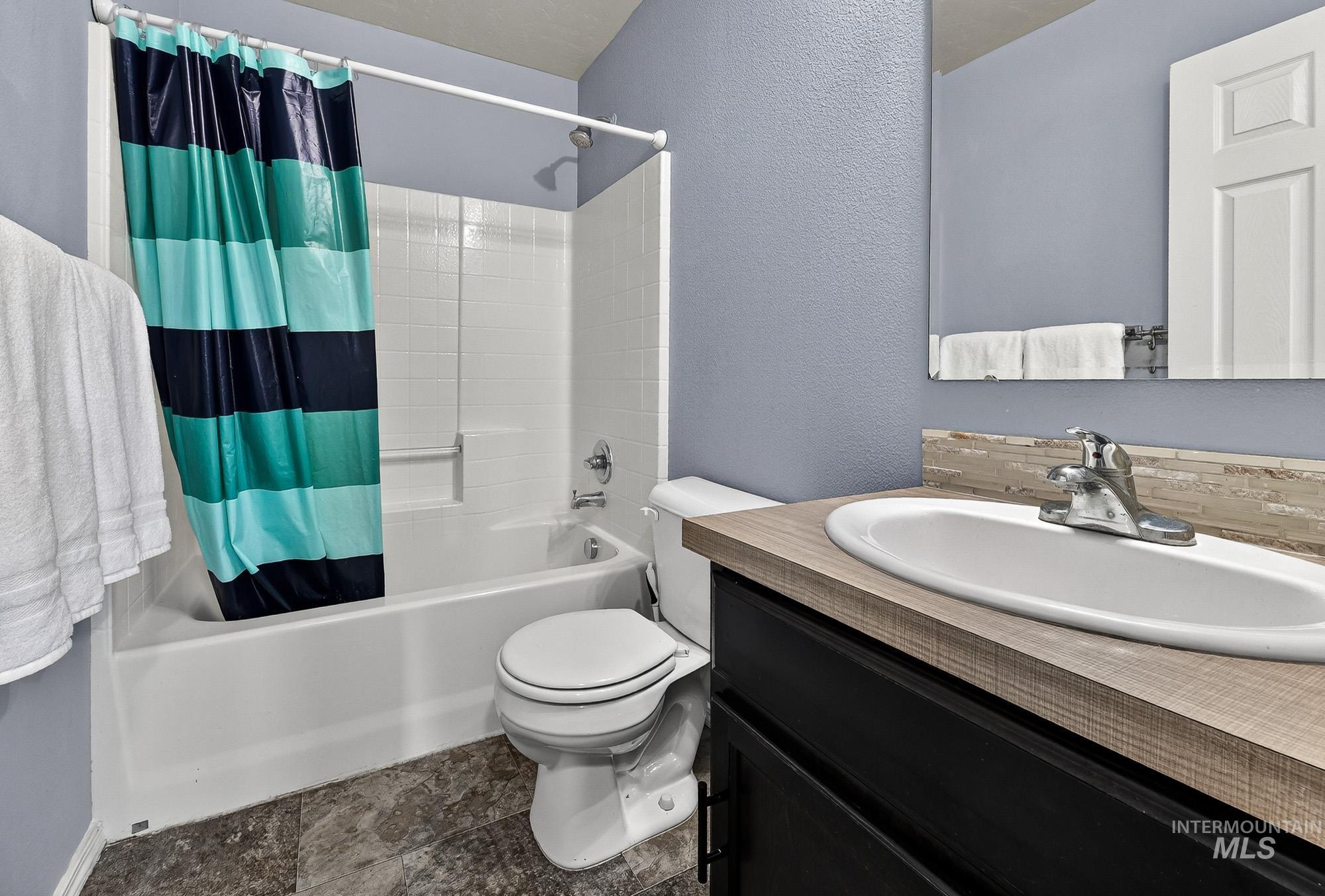 Full bathroom featuring shower / tub combo with curtain, a textured wall, vanity, and tasteful backsplash