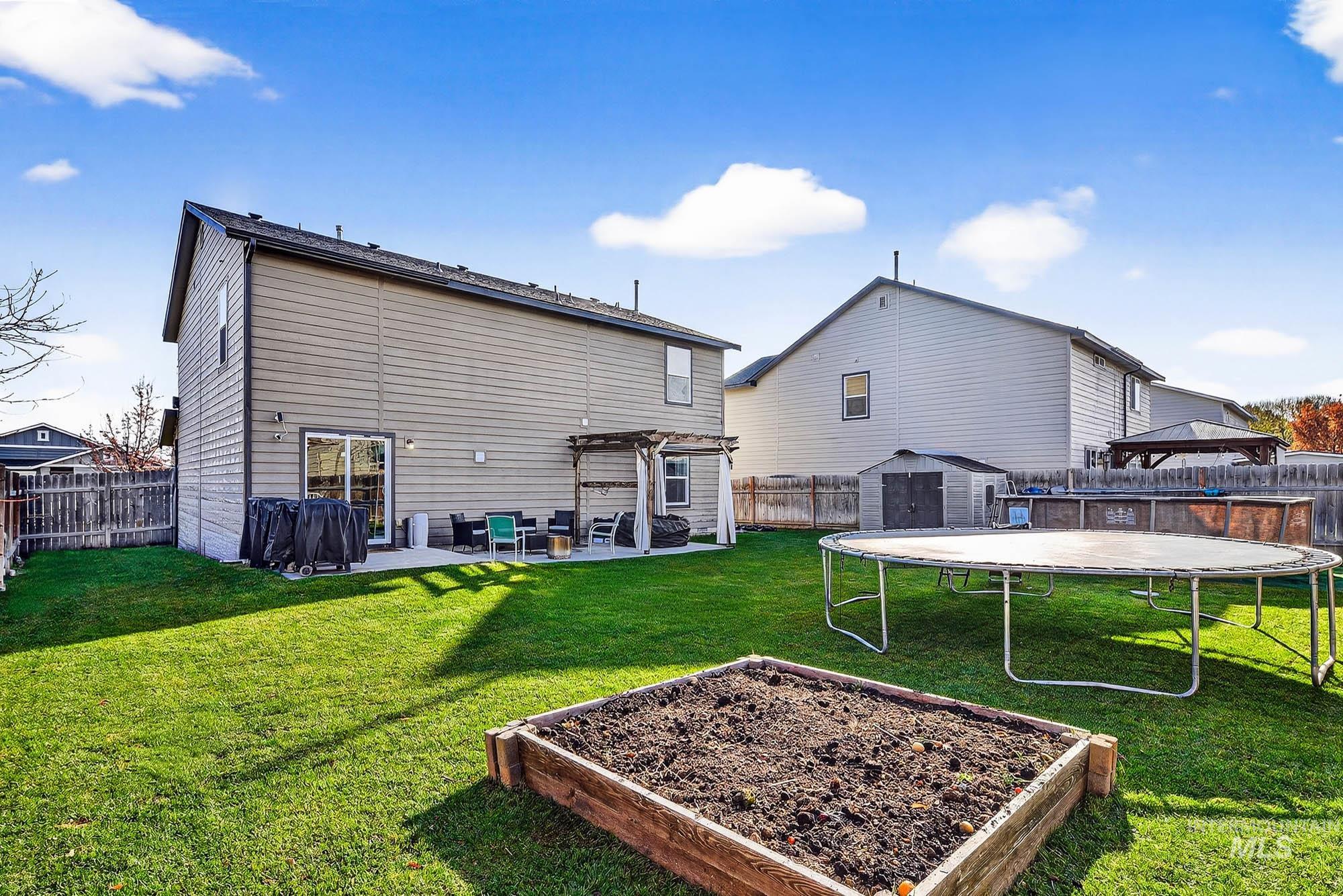 Back of property with a patio, a pergola, garden boxes, a fenced backyard, a shed, and a trampoline