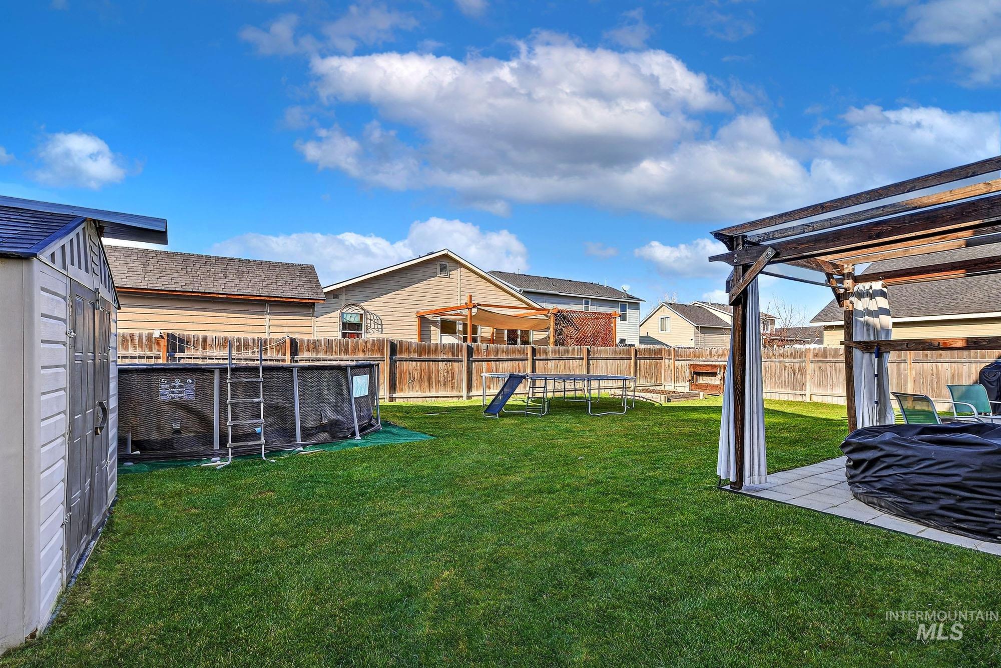 Fenced backyard with a trampoline, a pergola, a patio, and a residential view