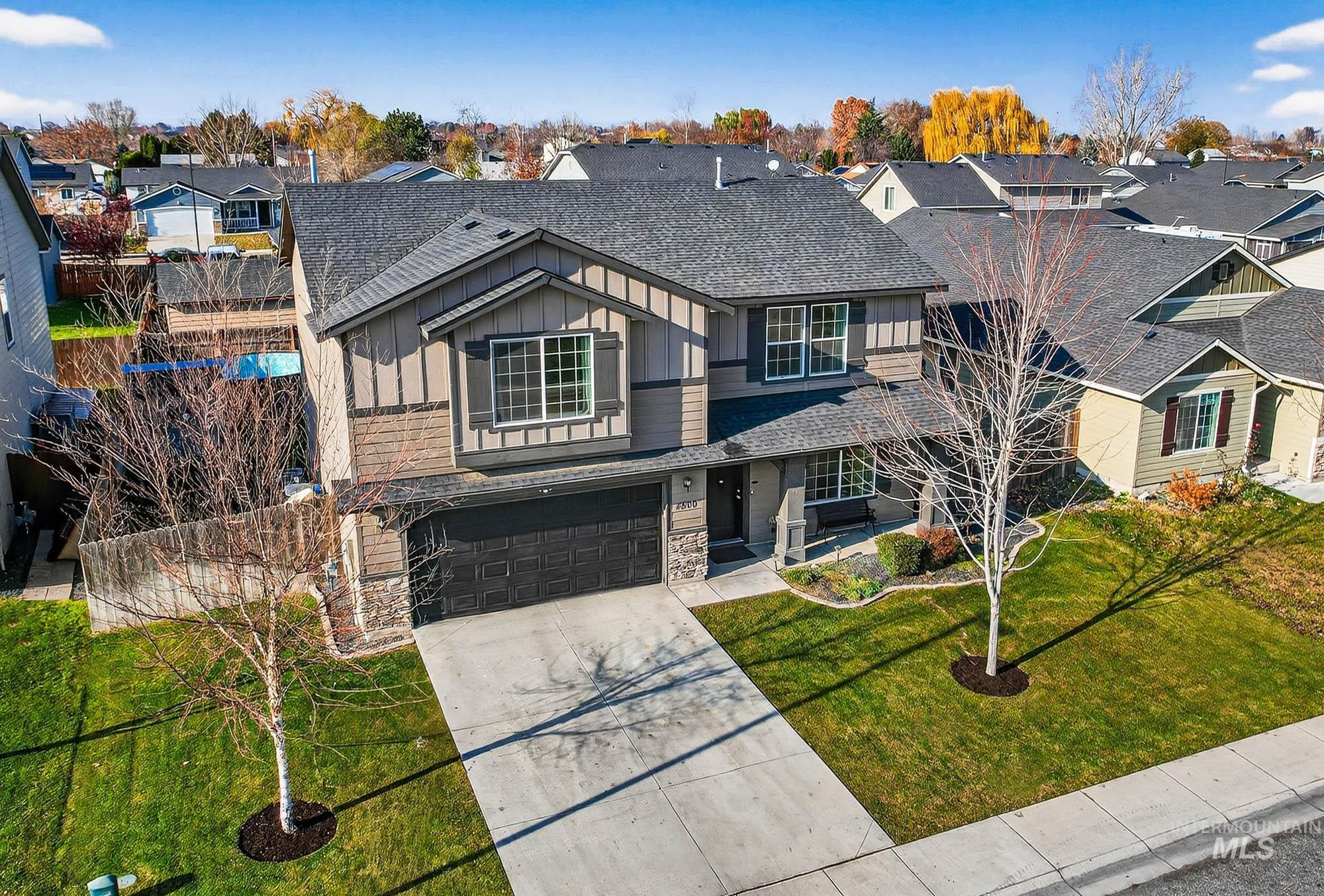 View of front of property featuring board and batten siding, a shingled roof, concrete driveway, a residential view, and stone siding