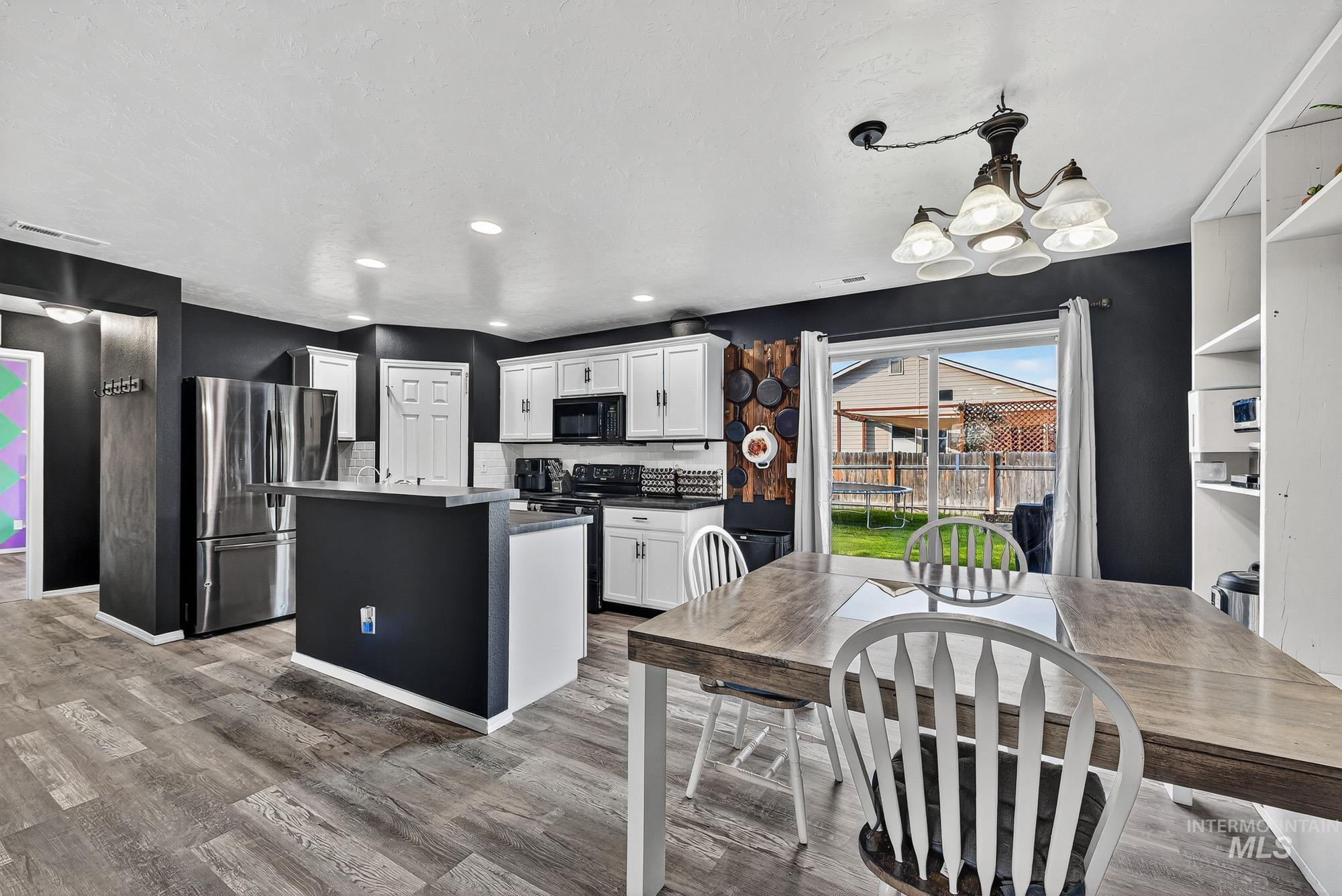 Kitchen with dark countertops, an island with sink, black appliances, white cabinets, and a chandelier