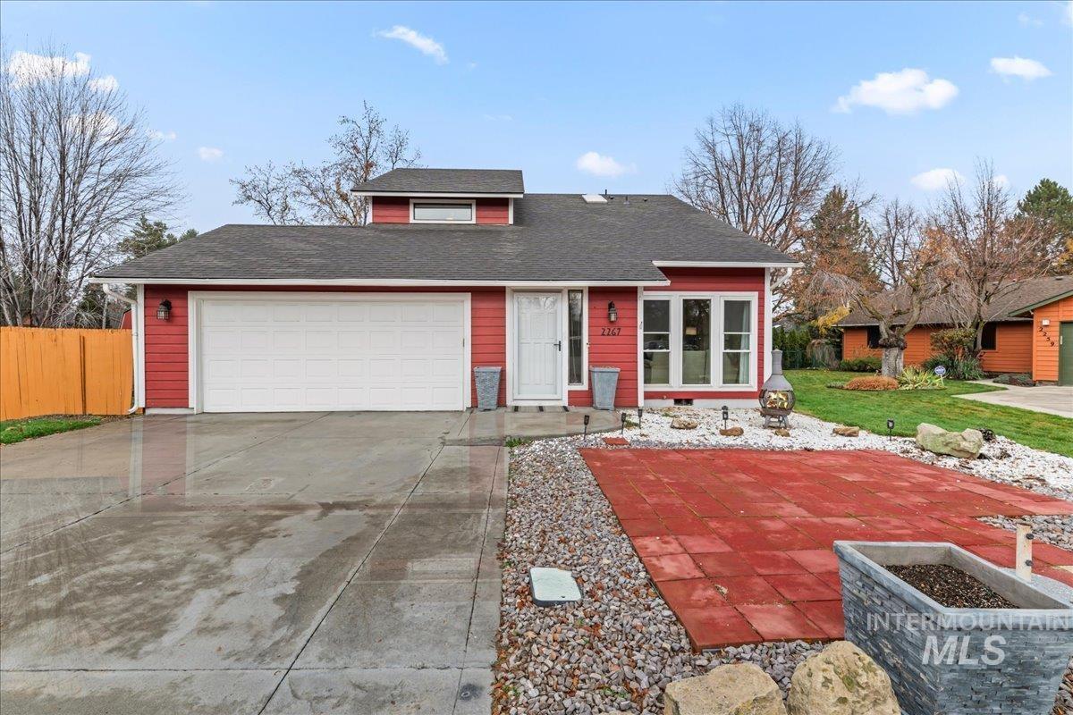 View of front of property featuring concrete driveway, a shingled roof, a garage, and a patio area