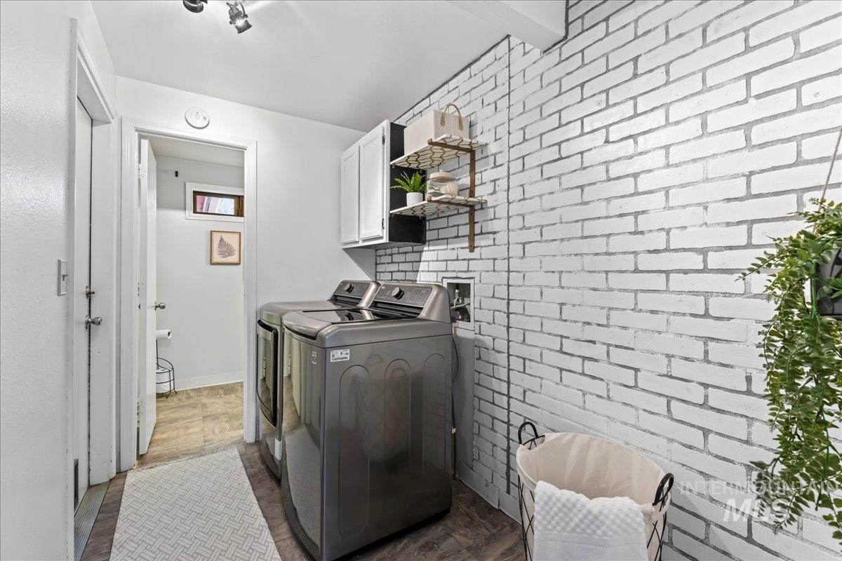 Laundry room with brick wall, dark wood-type flooring, cabinet space, and washing machine and dryer