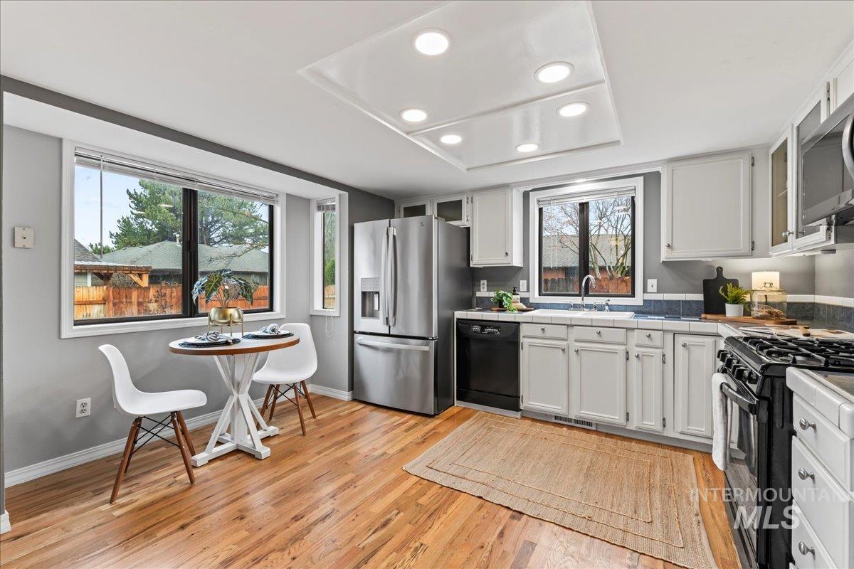 Kitchen featuring white cabinets, tile counters, black appliances, and light wood-type flooring
