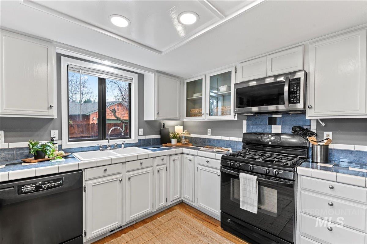 Kitchen with black appliances, white cabinetry, tile countertops, and light wood-style floors