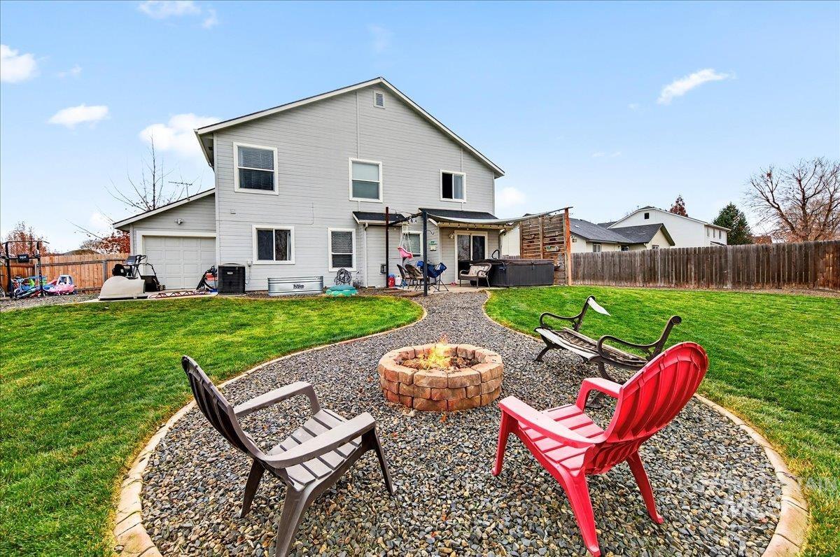 Back of property featuring a hot tub, a patio area, a fenced backyard, a fire pit, and a garage