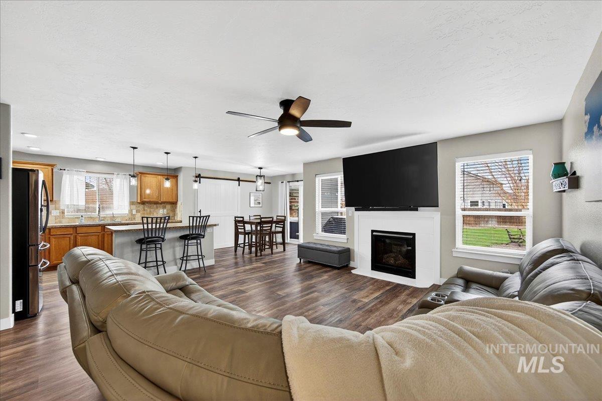 Living room with a ceiling fan, a glass covered fireplace, dark wood-style floors, a barn door, and a textured ceiling