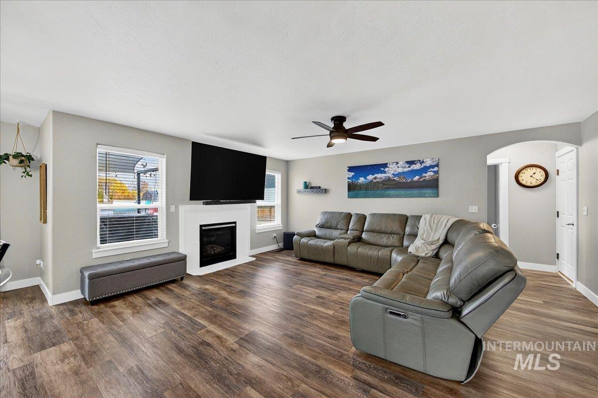 Living room with arched walkways, a ceiling fan, a fireplace with flush hearth, and dark wood finished floors