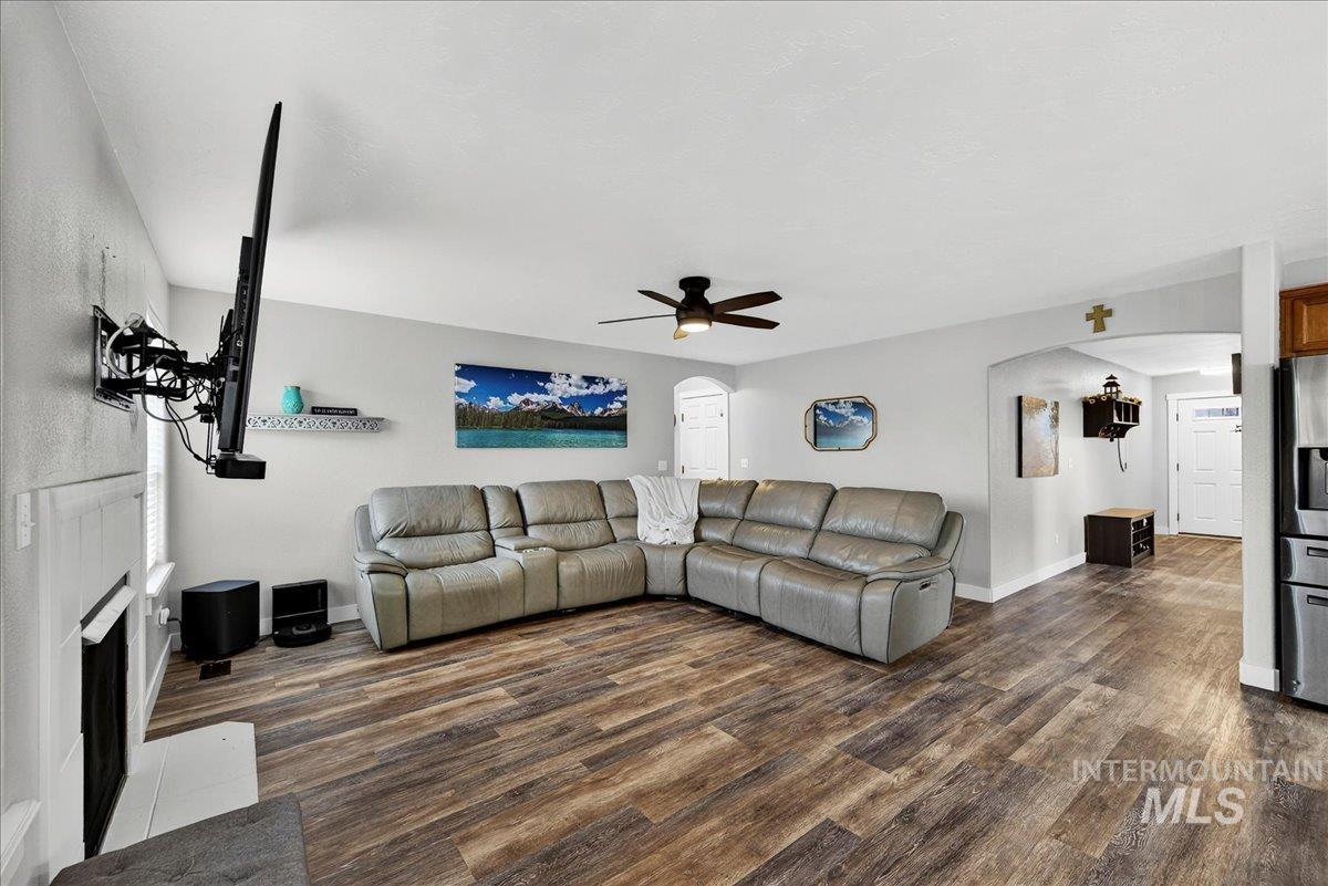 Living room with arched walkways, ceiling fan, a fireplace, and dark wood-style flooring
