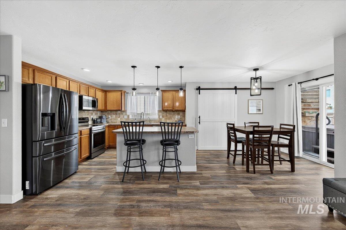 Kitchen featuring stainless steel appliances, a center island, a barn door, brown cabinets, and pendant lighting