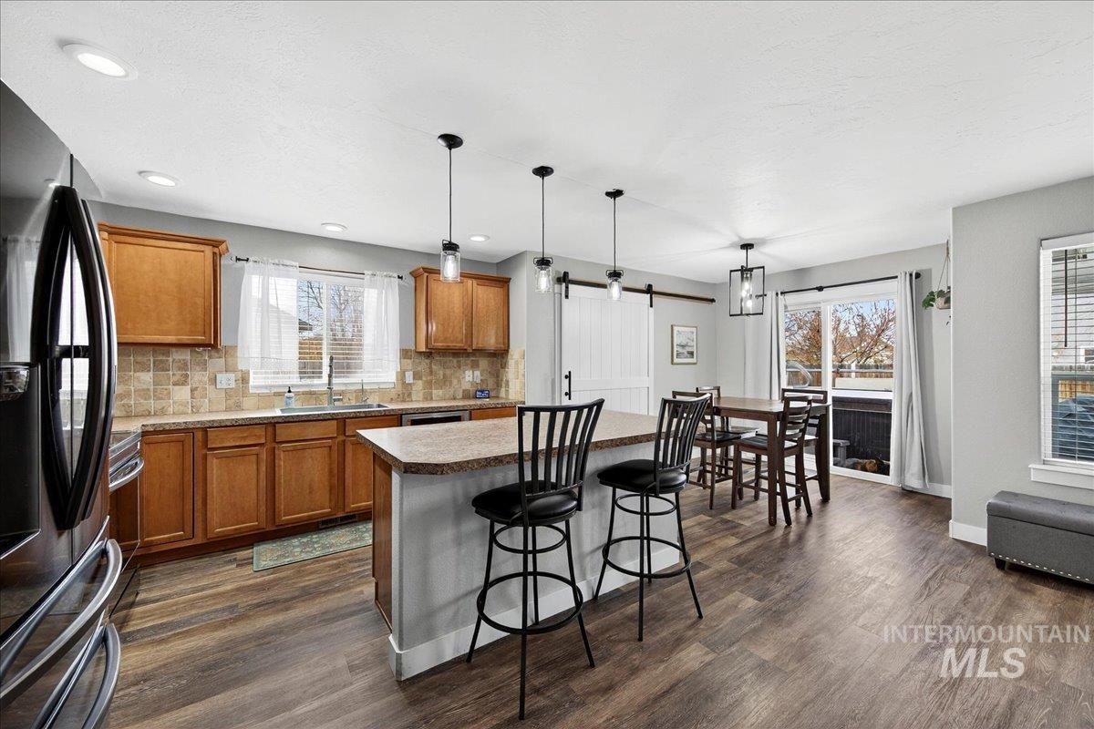 Kitchen featuring brown cabinets, black refrigerator with ice dispenser, backsplash, a kitchen bar, and recessed lighting