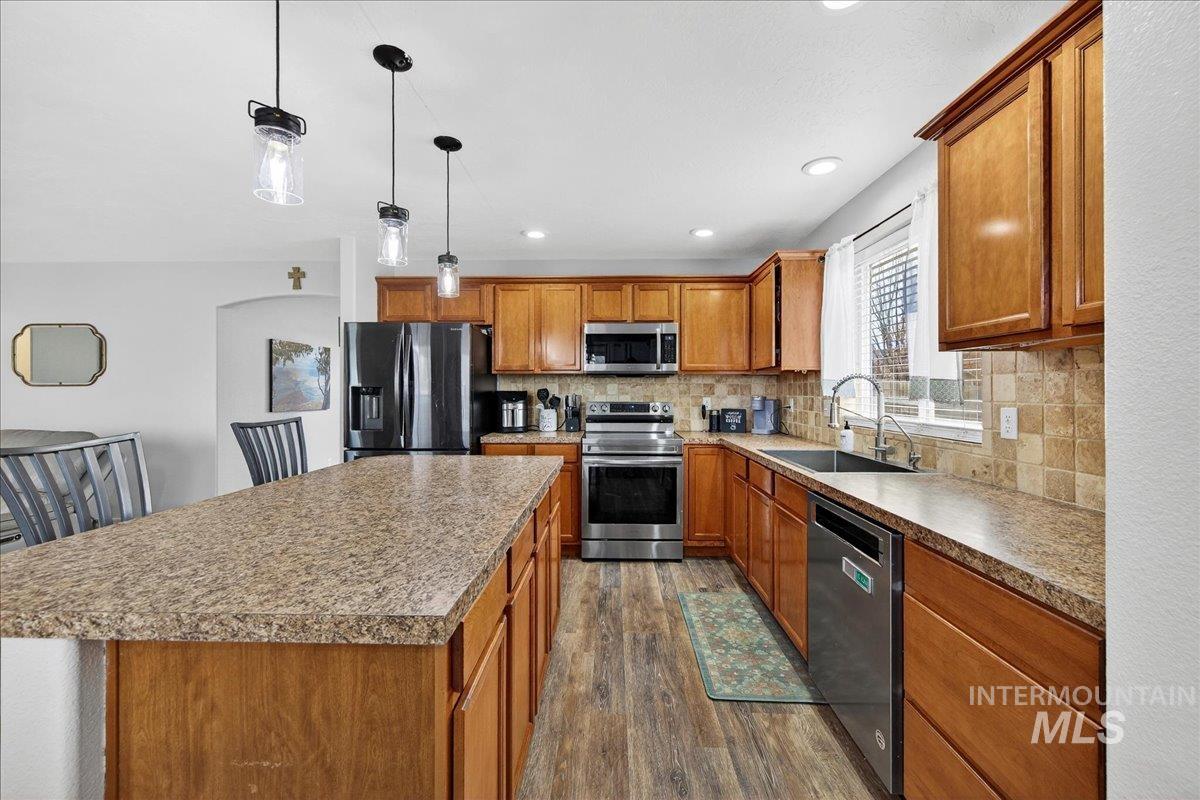 Kitchen with brown cabinets, decorative light fixtures, appliances with stainless steel finishes, a center island, and decorative backsplash