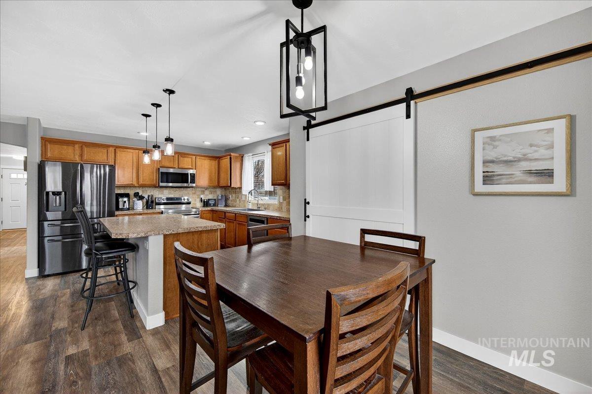 Dining room with a barn door, dark wood-style flooring, and recessed lighting