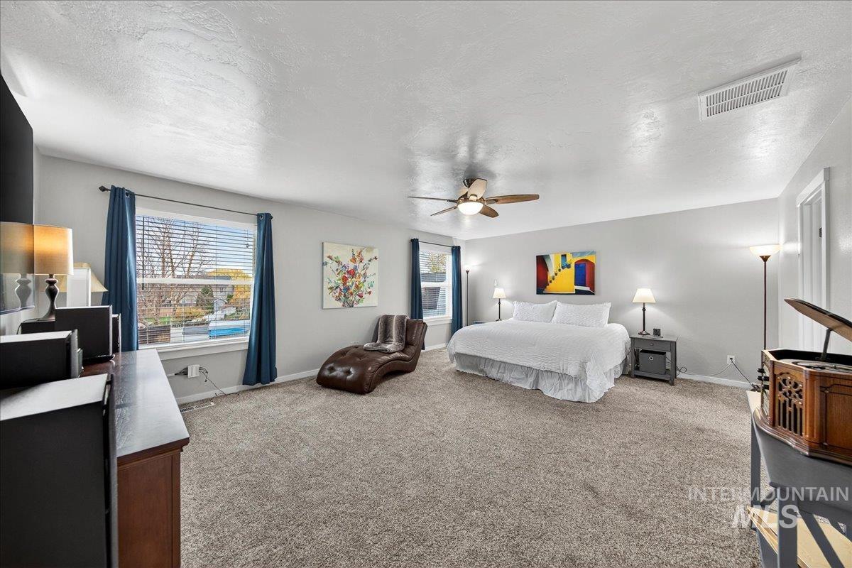 Bedroom featuring a textured ceiling, multiple windows, light colored carpet, and a ceiling fan