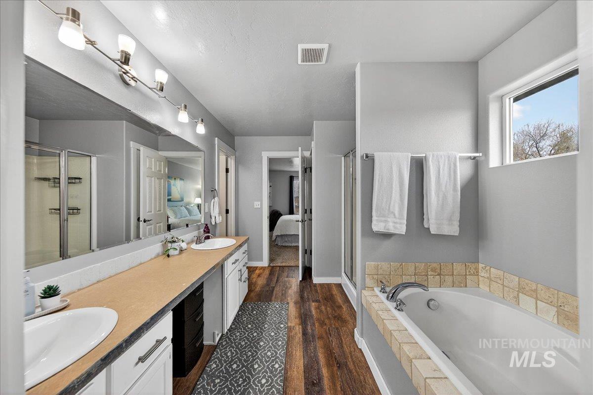 Ensuite bathroom featuring a stall shower, double vanity, a garden tub, and dark wood finished floors