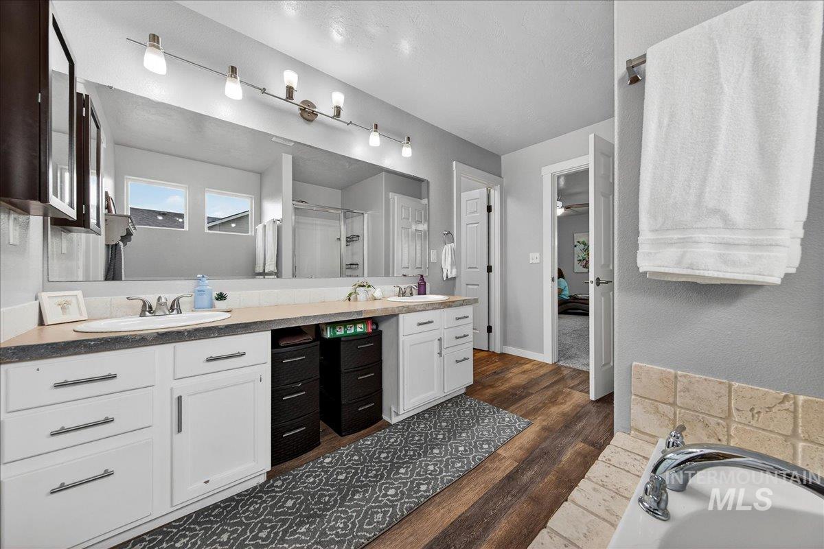 Full bathroom featuring double vanity, a shower stall, dark wood-style flooring, and a tub