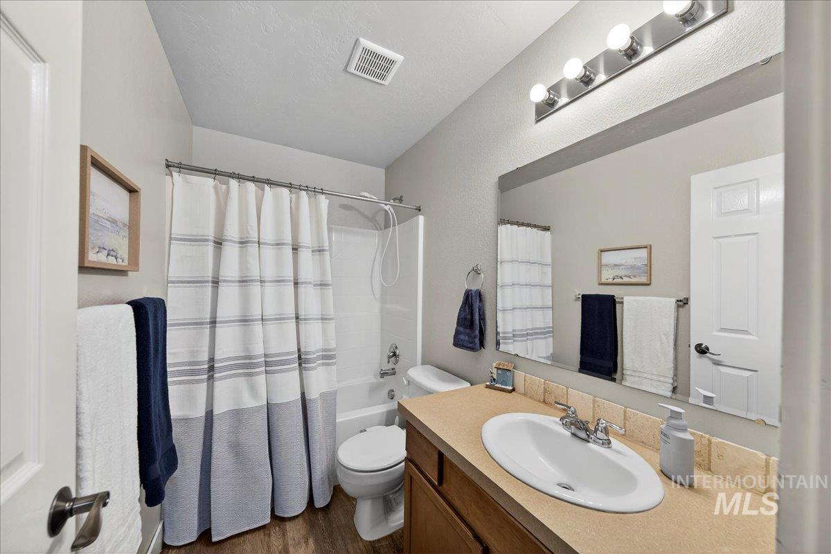 Bathroom featuring shower / bathtub combination with curtain, vanity, a textured ceiling, and dark wood-style floors