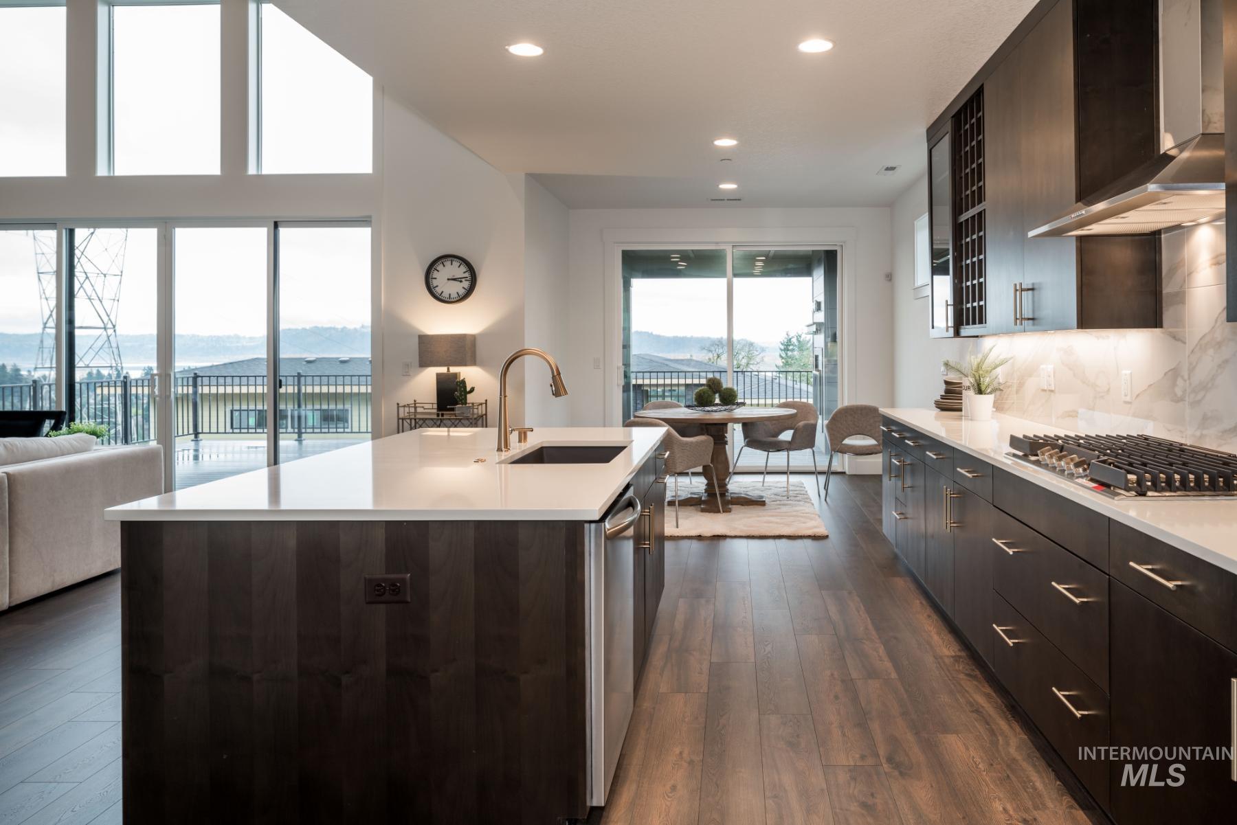 Kitchen with wall chimney range hood, dark wood finished floors, backsplash, open floor plan, and dark brown cabinets
