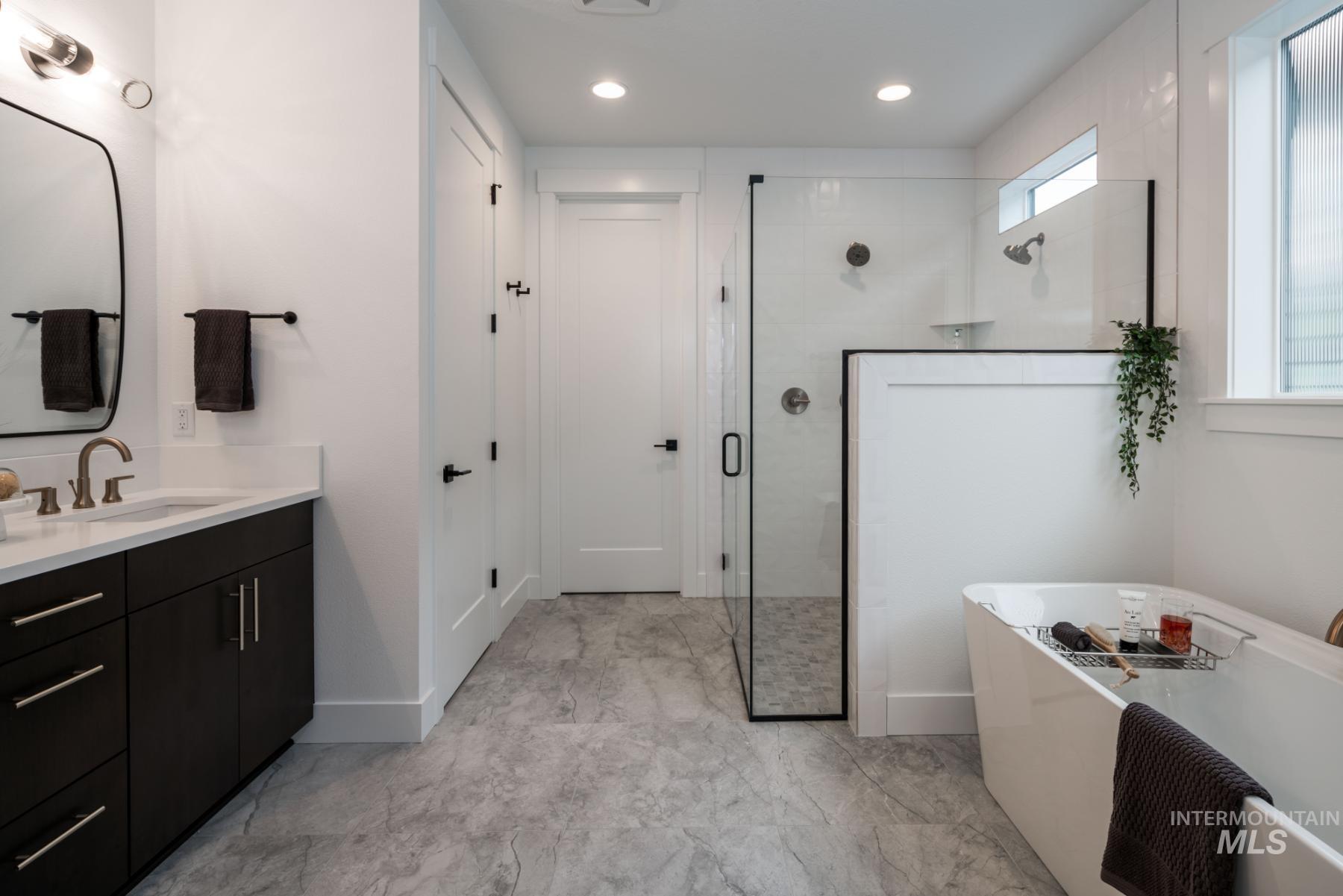 Bathroom featuring vanity, a freestanding tub, a shower stall, recessed lighting, and light marble finish flooring
