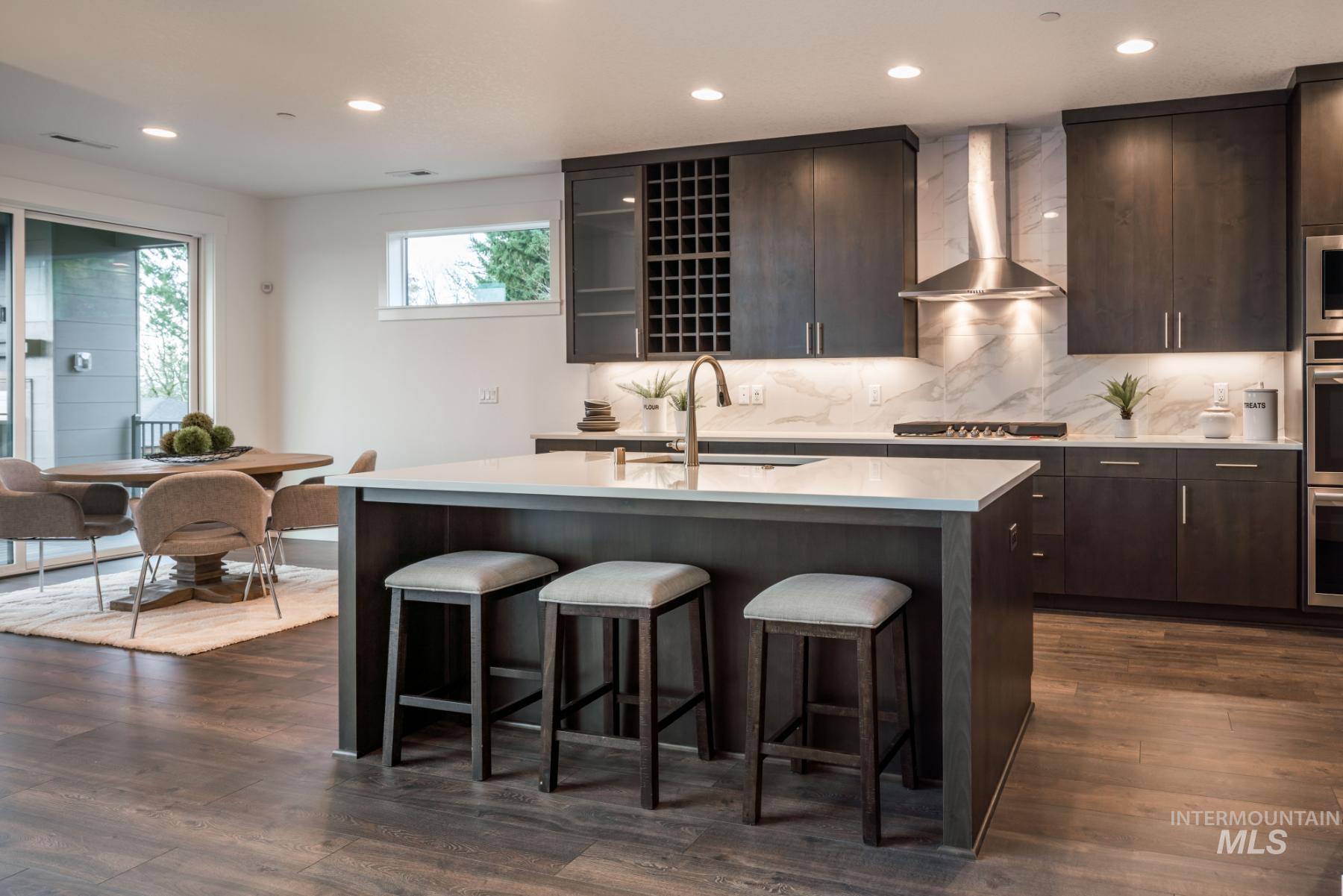 Kitchen featuring wall chimney exhaust hood, a center island with sink, a kitchen bar, recessed lighting, and light stone counters