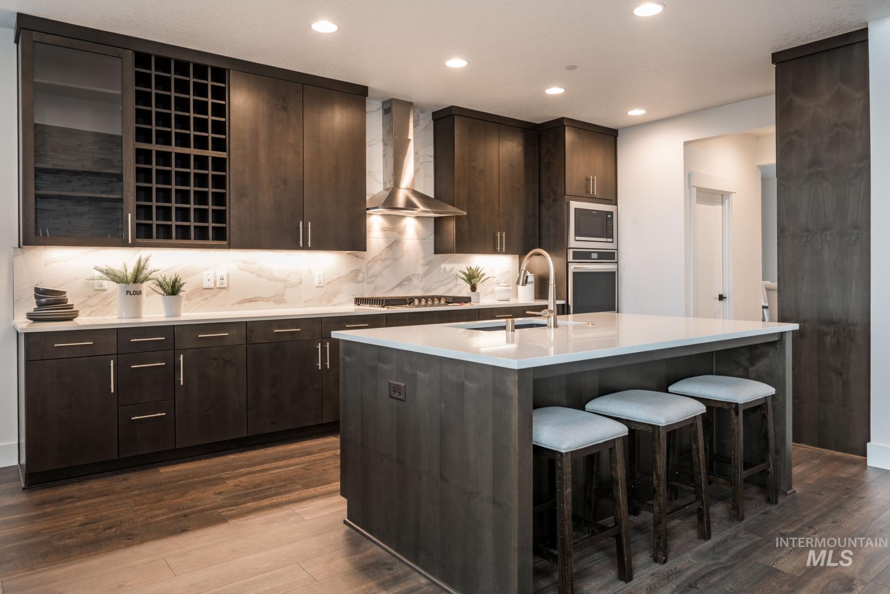 Kitchen featuring dark brown cabinetry, light stone counters, a kitchen bar, wall chimney exhaust hood, and recessed lighting