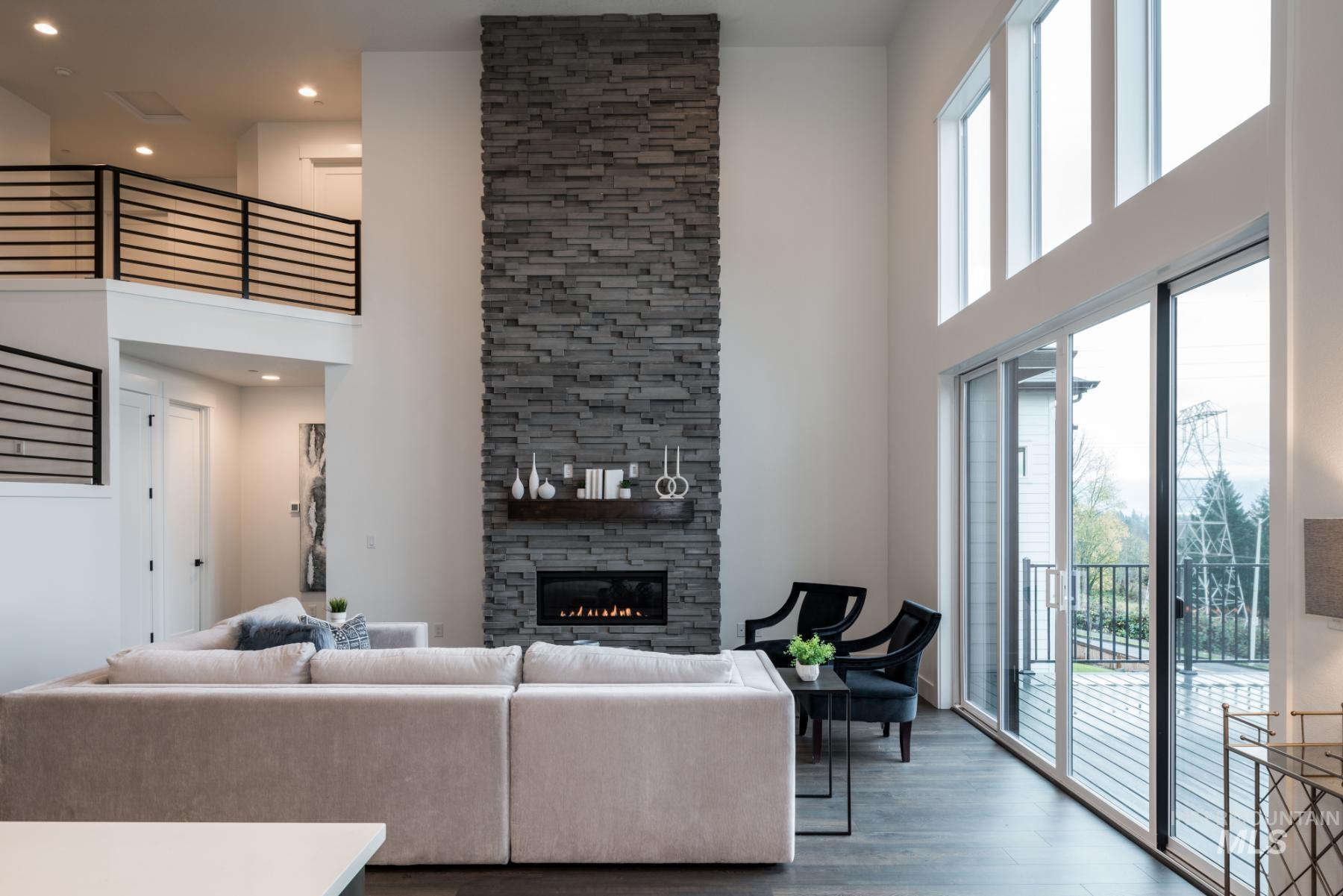 Living area with a towering ceiling, a stone fireplace, wood finished floors, and recessed lighting