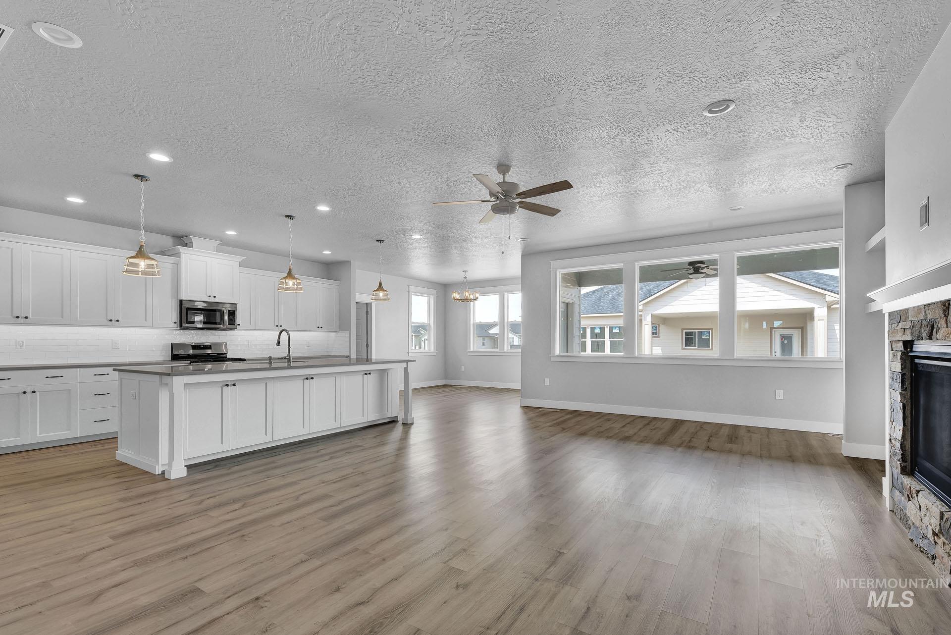 Unfurnished living room featuring ceiling fan, a fireplace, a textured ceiling, light wood finished floors, and recessed lighting