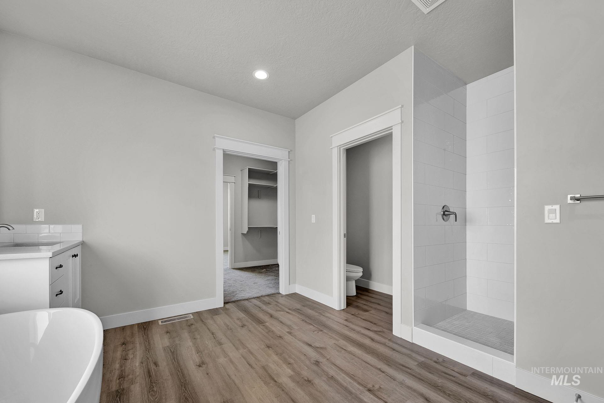 Bathroom featuring vanity, a freestanding tub, tiled shower, a walk in closet, and light wood-type flooring