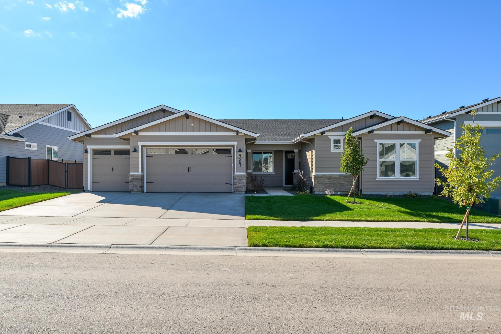Craftsman-style home featuring board and batten siding, stone siding, an attached garage, and a front lawn