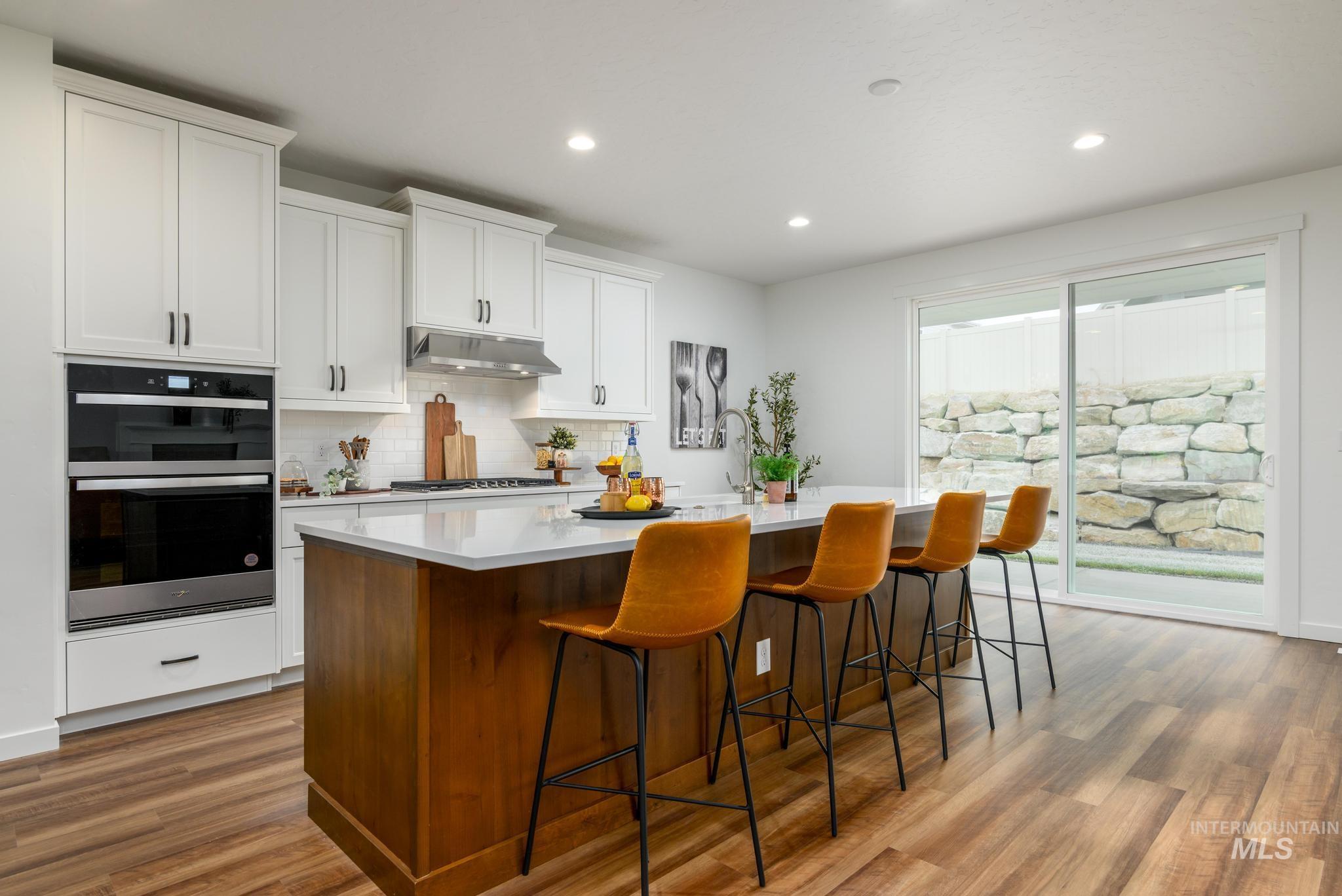 Kitchen featuring a center island with sink, a breakfast bar, white cabinetry, stainless steel double oven, and recessed lighting
