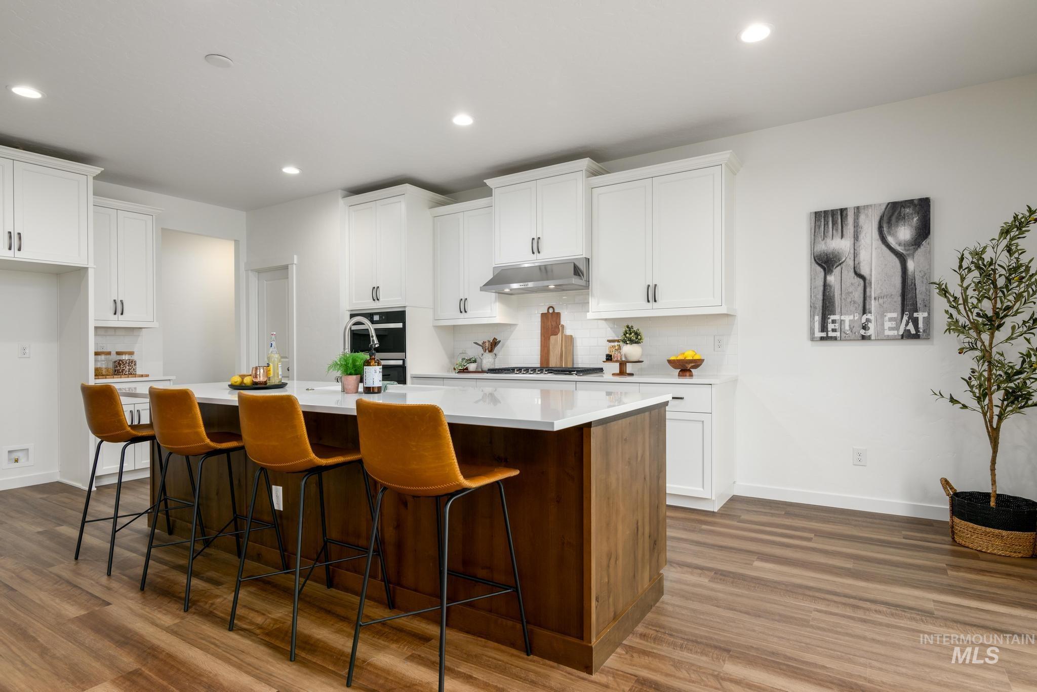 Kitchen featuring white cabinets, an island with sink, a breakfast bar area, tasteful backsplash, and recessed lighting