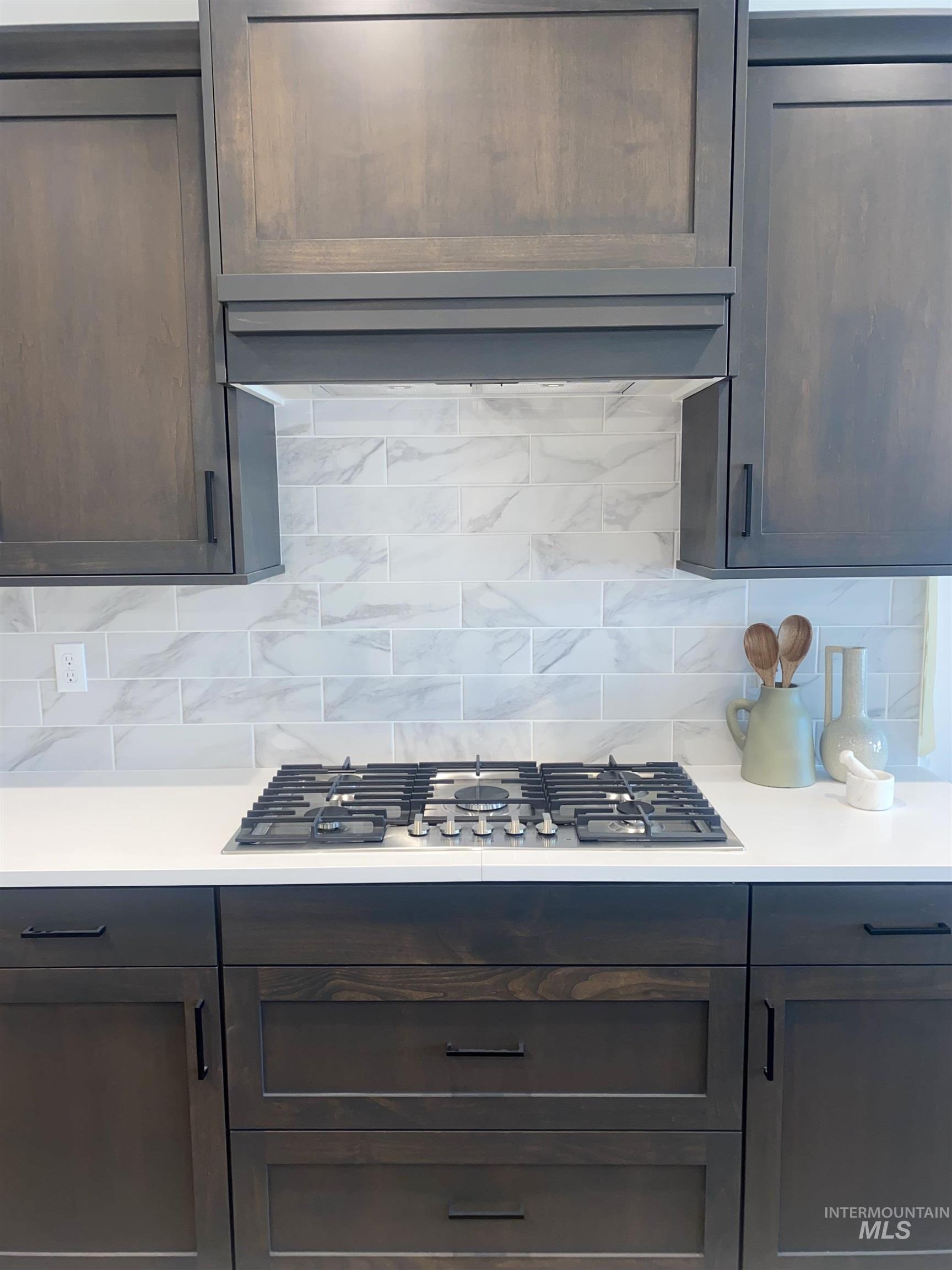 Kitchen with tasteful backsplash, stainless steel gas cooktop, exhaust hood, and dark brown cabinetry