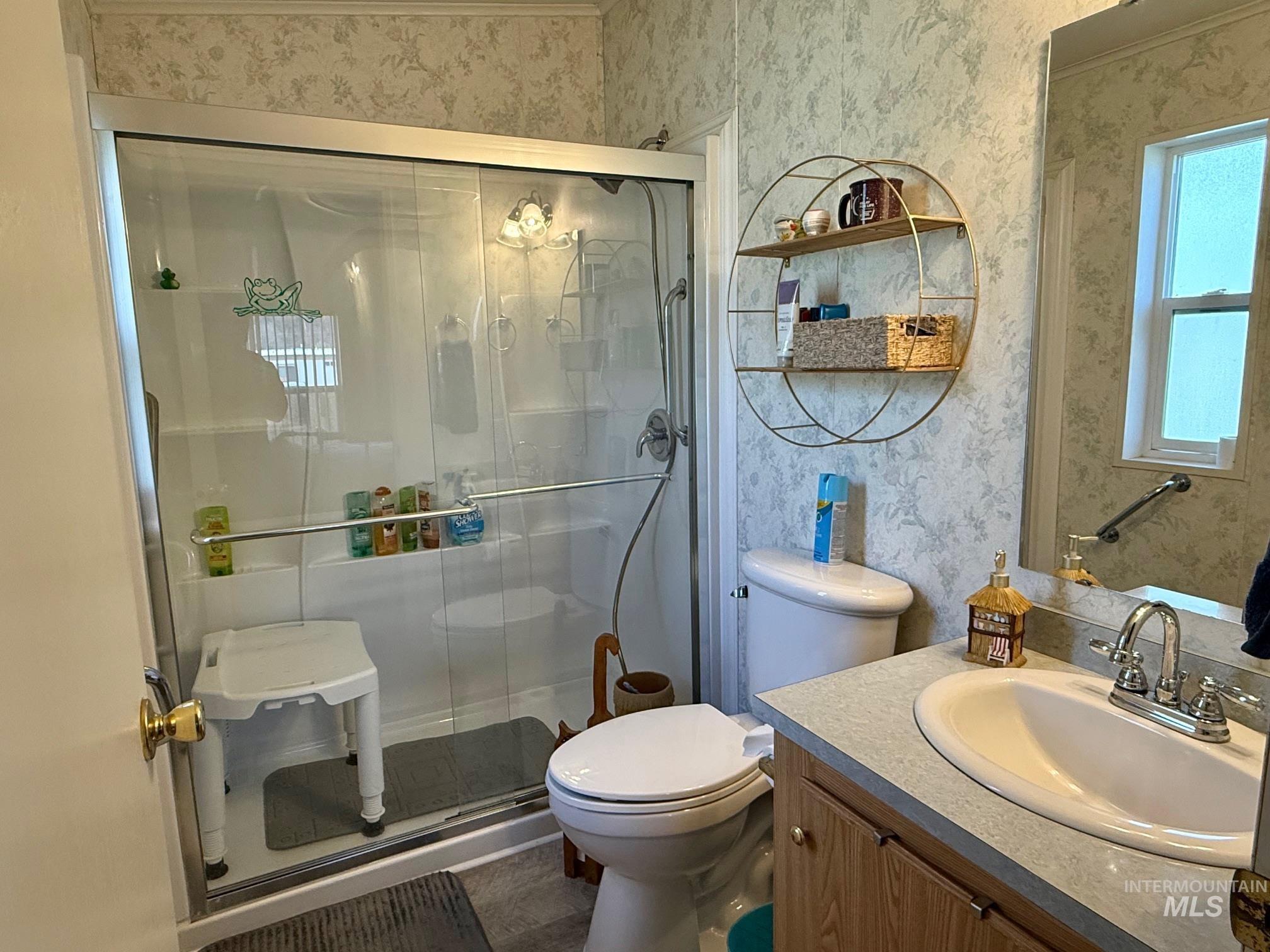 Bathroom with vanity, wallpapered walls, and a shower stall