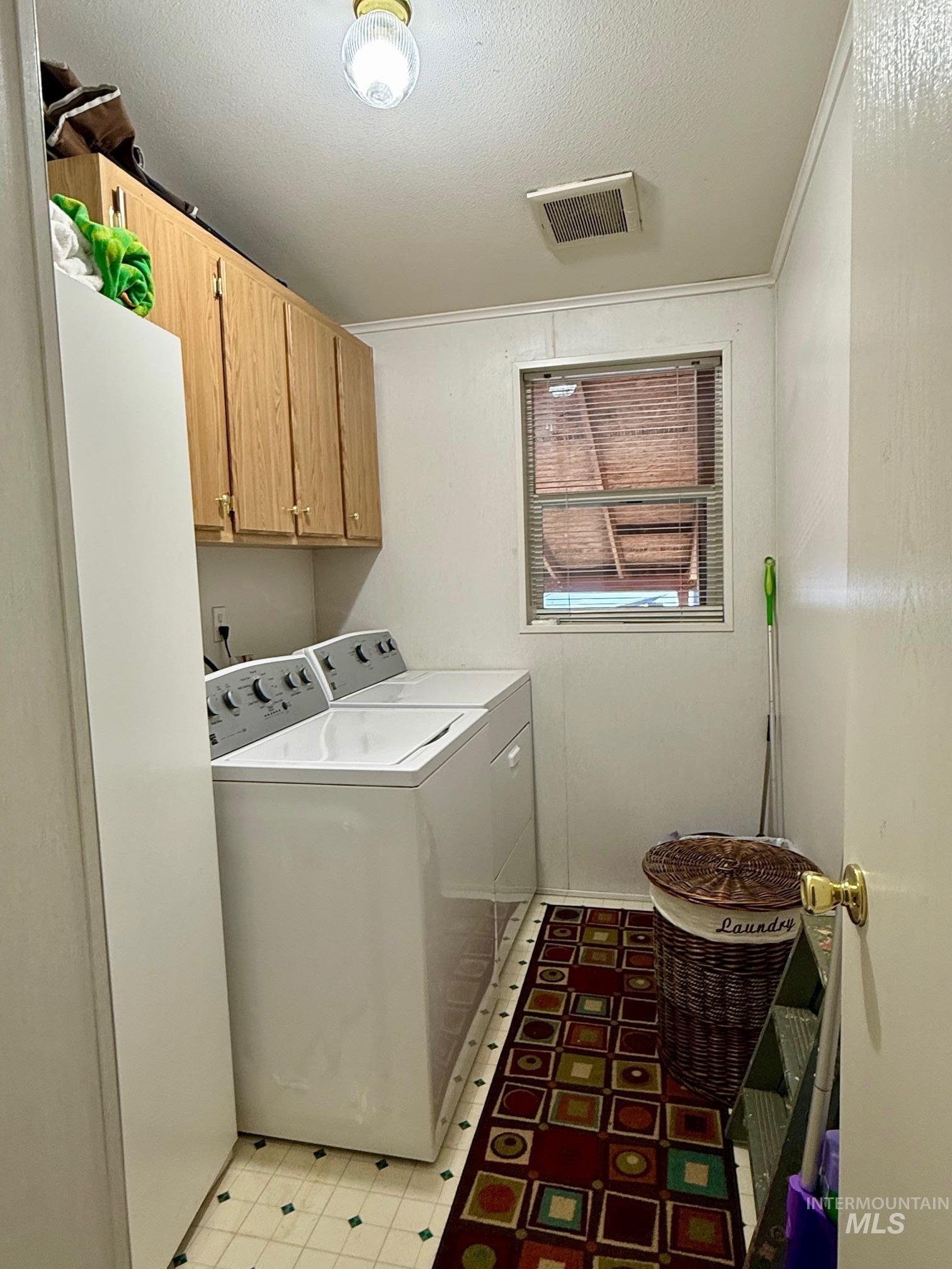 Laundry room with cabinet space, a textured ceiling, independent washer and dryer, light floors, and crown molding